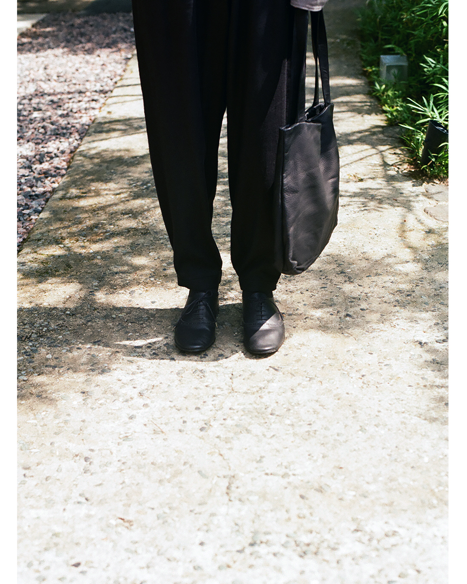 Black deer leather shoulder tote bag carried at side while walking, soft texture and minimal form, VU