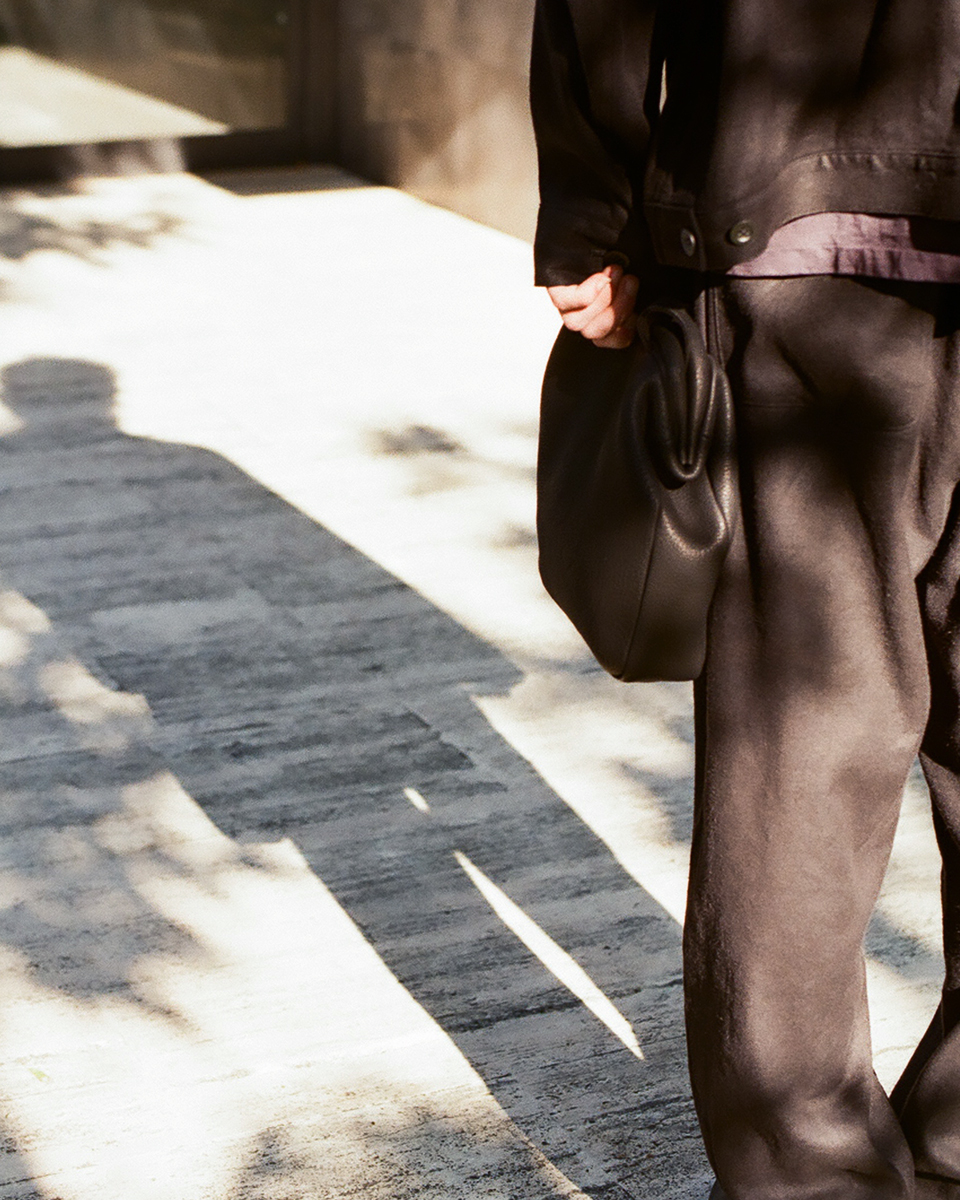 Black deer leather kiss-lock shoulder bag carried by hand, soft drape and natural movement, VU