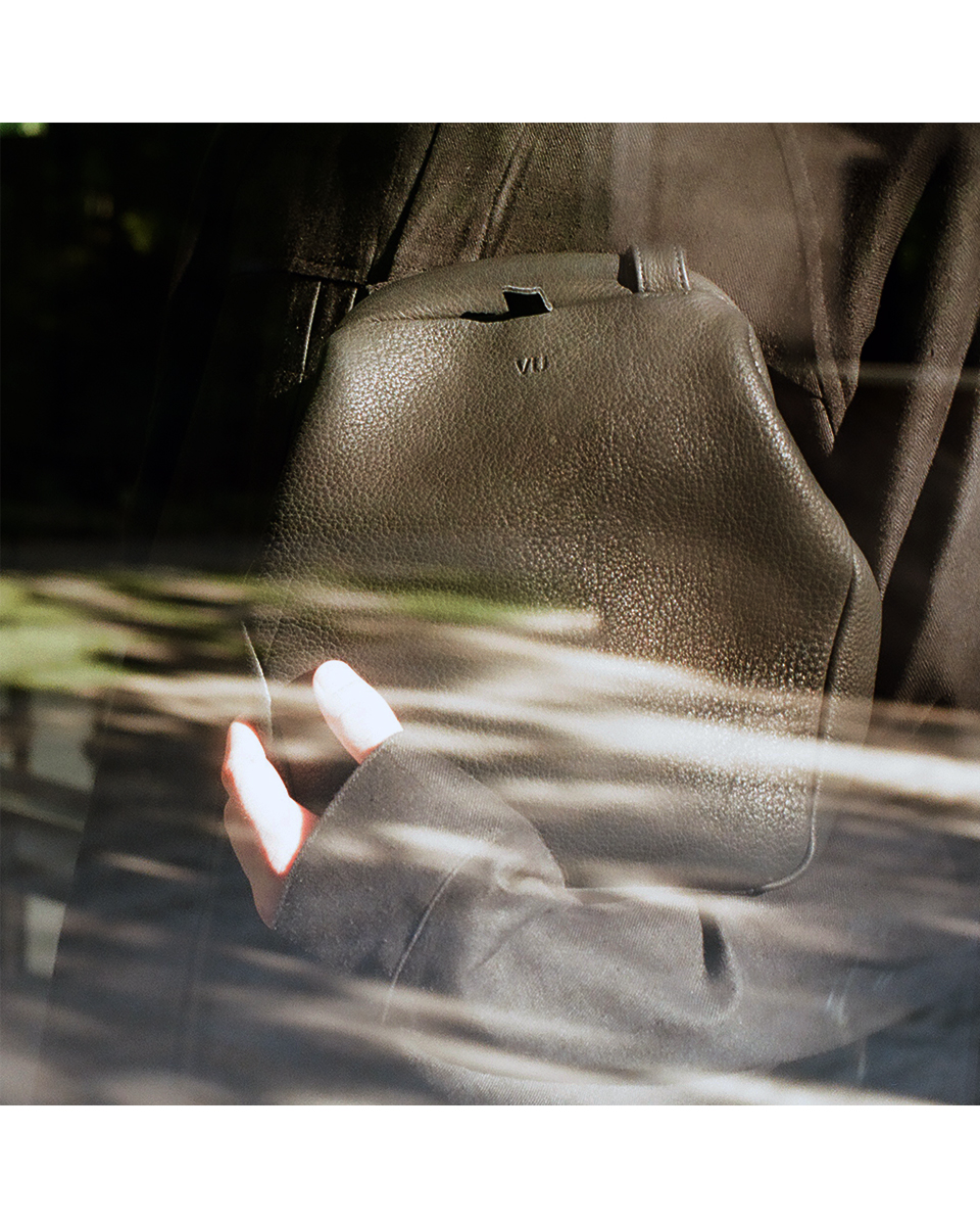Deer leather kiss-lock shoulder bag held in hand, soft texture and natural light, VU minimal design